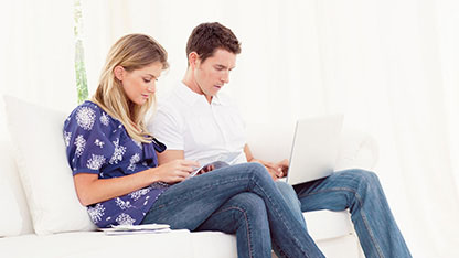 Man and woman sat on sofa researching bank accounts