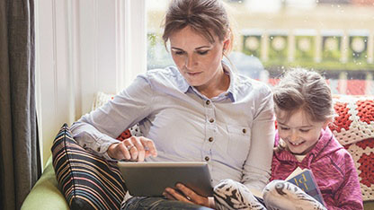 Lady using laptop on sofa with young girl sat next to her