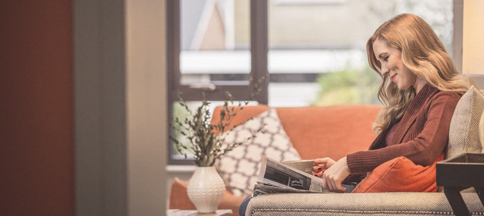 Woman reading a magazine sat on her sofa at home